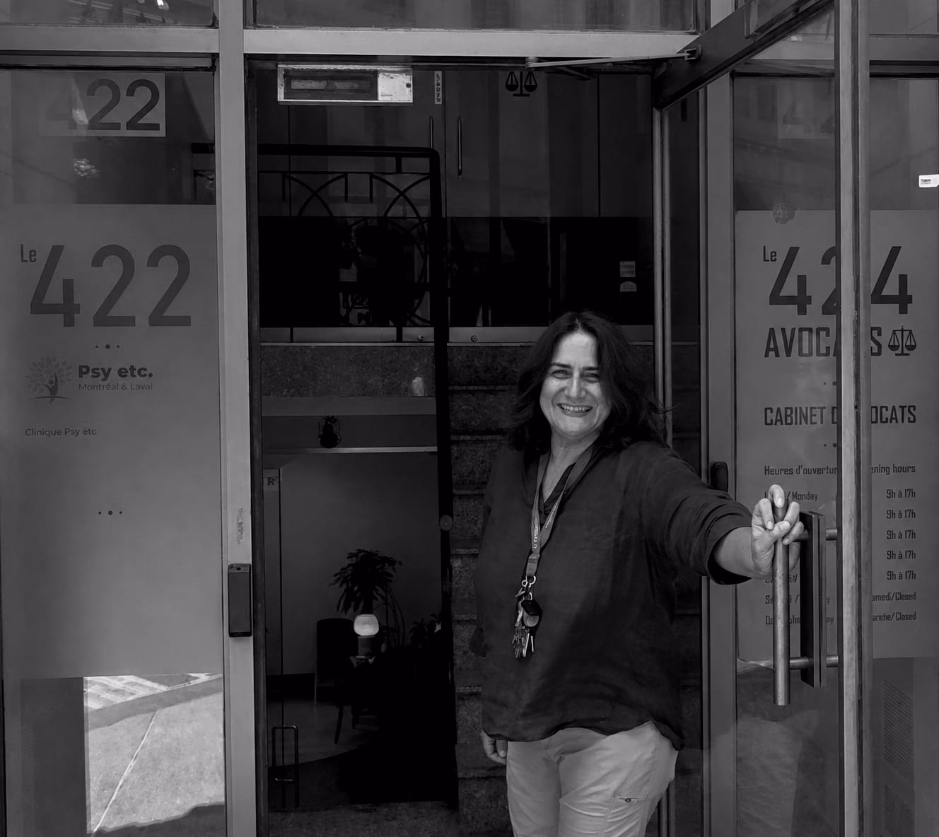 Jacqueline Hilaire tient ouverte la porte vitrée de la clinique de Montréal. Sur le vitrage à sa droite, l’enseigne « Le 422 » et le logo de la clinique ; derrière elle, l’escalier et un fauteuil du hall.