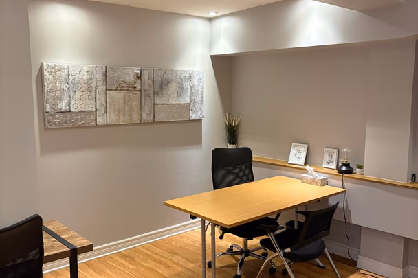 Une salle de réunion avec une table claire, deux chaises de bureau, un triptyque de toiles beiges au mur et un plancher de bois blond.