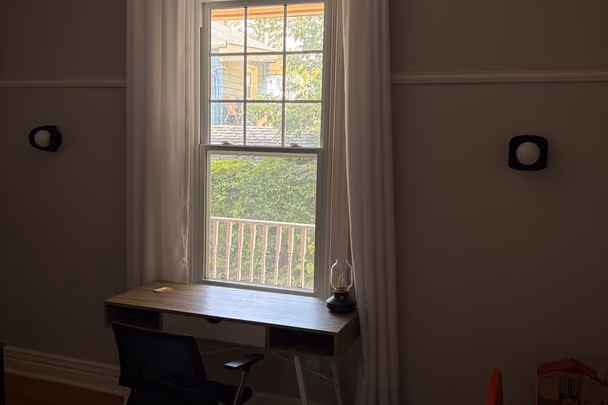 Un bureau avec une table de travail devant une haute fenêtre à rideaux, une chaise de bureau, et un coin de jeux pour enfants dans l'angle.