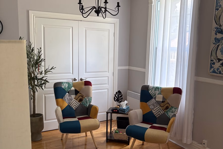 Une pièce de réception avec quatre fauteuils bariolés autour de deux guéridons, un lustre à pampilles et de hautes portes à moulures blanches.