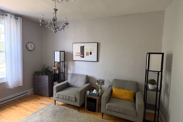 Un bureau avec deux fauteuils vert d'eau, dont l'un porte un coussin jaune, séparés par un guéridon, un lustre à pampilles, une toile abstraite et deux étagères noires.